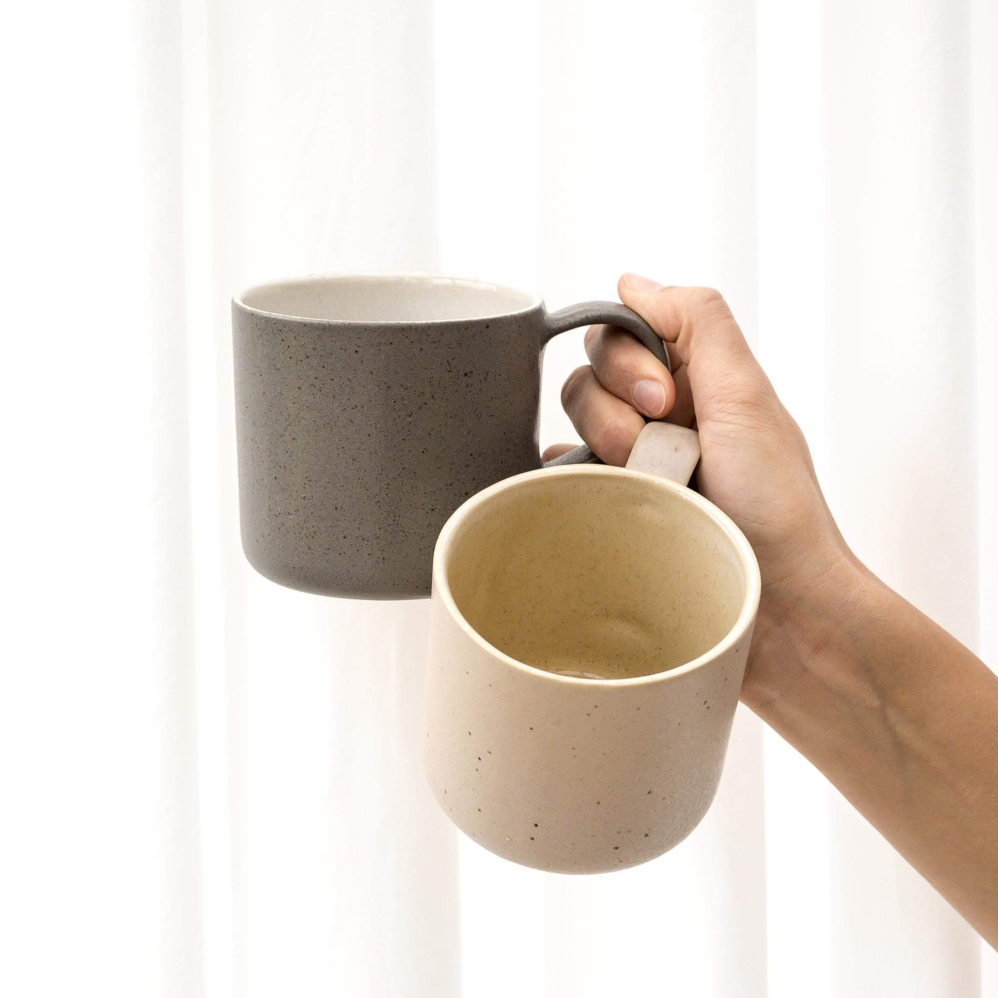 Steingut Tasse in Beige und Grau von rechter Hand hochgehalten.