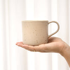 Steingut Tasse in Beige auf linker Hand.